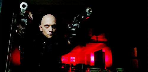Victor Zsasz from Gotham walking down a red-lit hall, both guns drawn.